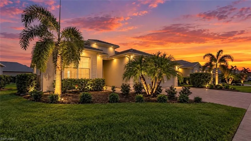 Exterior featuring stucco siding, lush tropical landscaping, and a concrete paver driveway