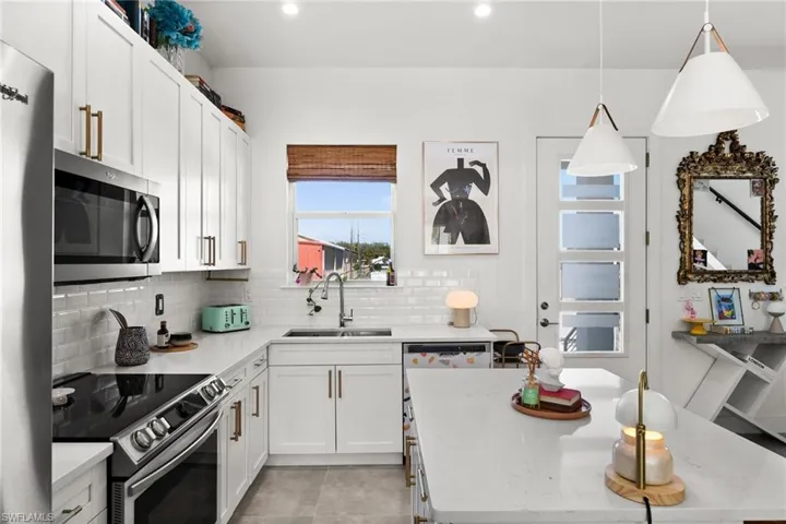 Kitchen with backsplash, stainless steel appliances, sink, white cabinetry, and hanging light fixtures