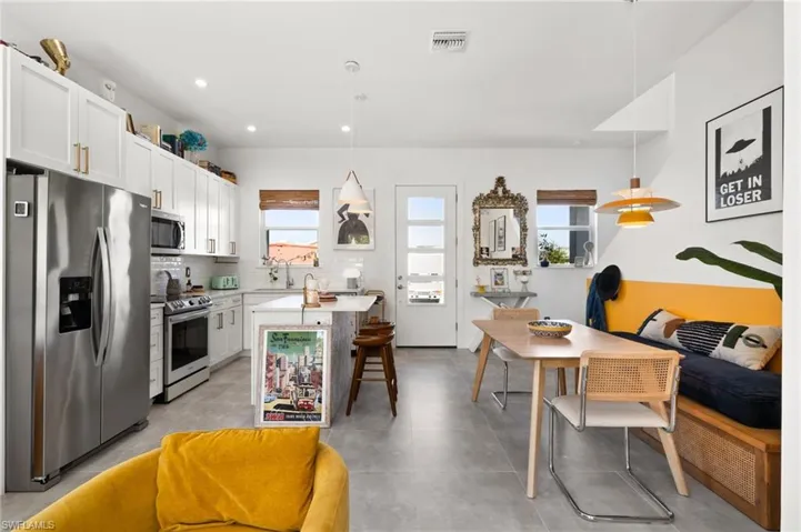 Kitchen with appliances with stainless steel finishes, backsplash, decorative light fixtures, white cabinetry, and a breakfast bar area