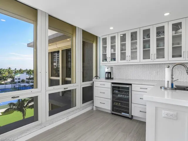 Bar featuring white cabinetry, light stone countertops, beverage cooler, tasteful backsplash, and glass insert cabinets