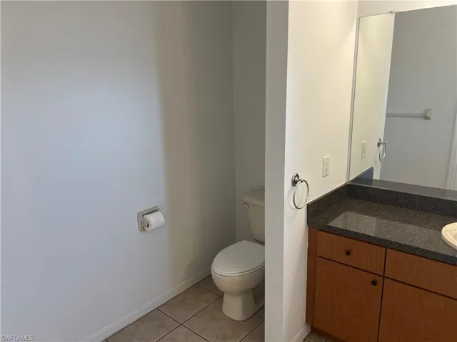 Half bath with vanity, toilet, baseboards, and tile patterned floors