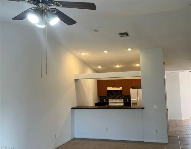 Kitchen with under cabinet range hood, tile patterned floors, white fridge with ice dispenser, and range