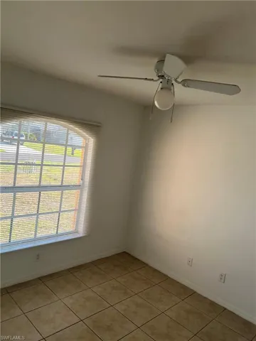 Empty room with light tile patterned floors, baseboards, and ceiling fan