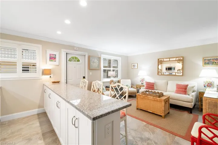 Kitchen featuring light stone counters, a breakfast bar area, crown molding and white cabinetry