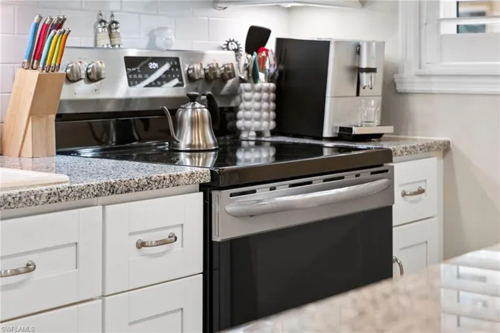 Kitchen with white cabinets, electric range, backsplash, and light stone counters