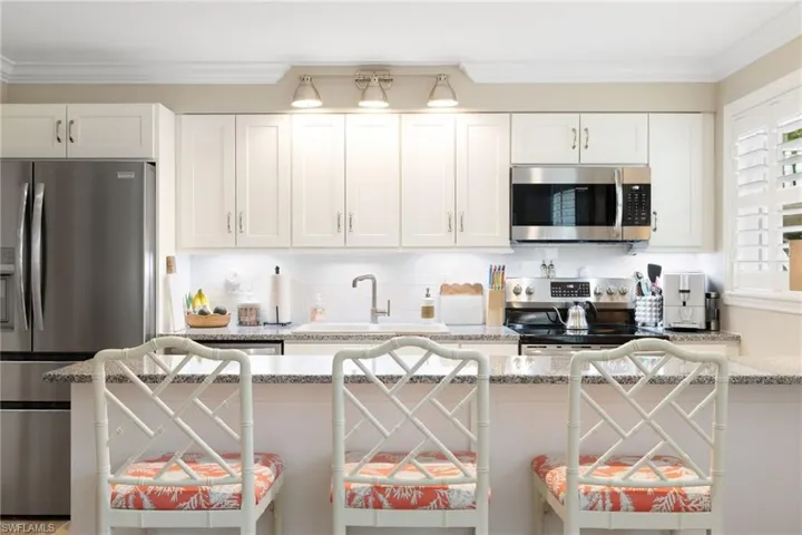 Kitchen featuring stainless steel appliances, a breakfast bar area, light stone counters, white cabinets, and ornamental molding