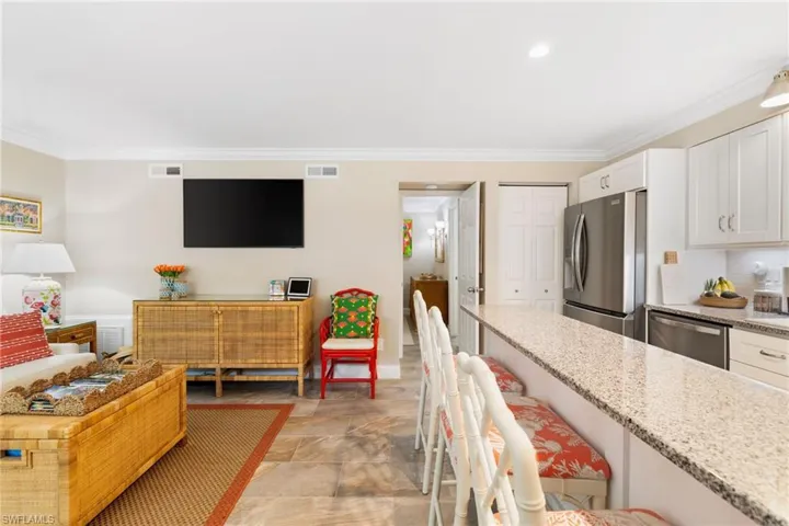 Kitchen featuring a breakfast bar, stainless steel appliances, white cabinets, ornamental molding, and light stone countertops