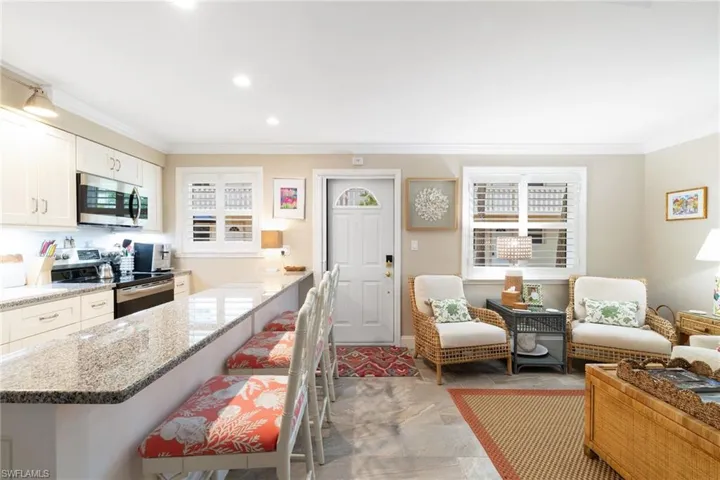 Kitchen featuring a kitchen bar, ornamental molding, white cabinets, stainless steel appliances, and light stone counters