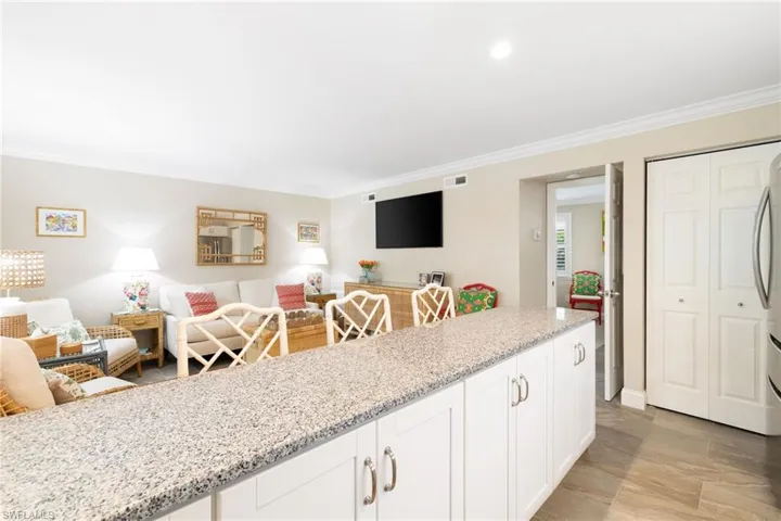 Kitchen featuring light stone countertops, white cabinets, crown molding and open floor plan
