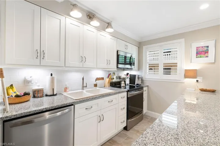 Kitchen with stainless steel appliances, white cabinets, backsplash, ornamental molding, and light stone counters