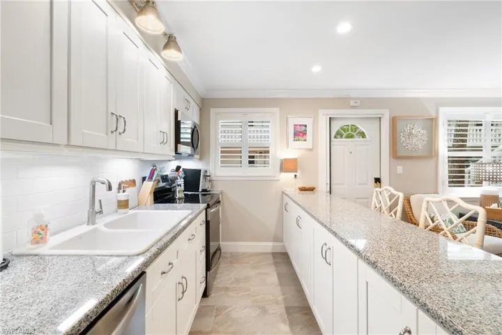 Kitchen with white cabinets, appliances with stainless steel finishes, light stone countertops, crown molding, and recessed lighting