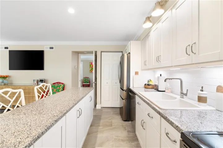 Kitchen with white cabinets, light stone countertops, appliances with stainless steel finishes, ornamental molding, and a breakfast bar