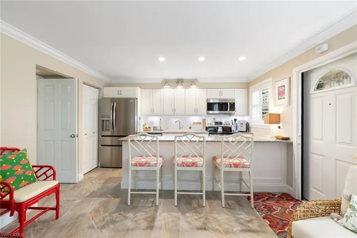 Kitchen with a kitchen bar, stainless steel appliances, white cabinetry, and light stone countertops
