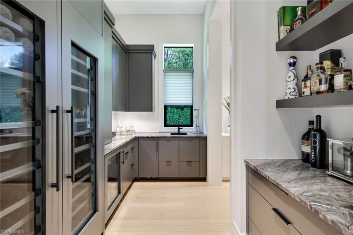 Kitchen with gray cabinets, a sink, open shelves, light stone countertops, and beverage cooler