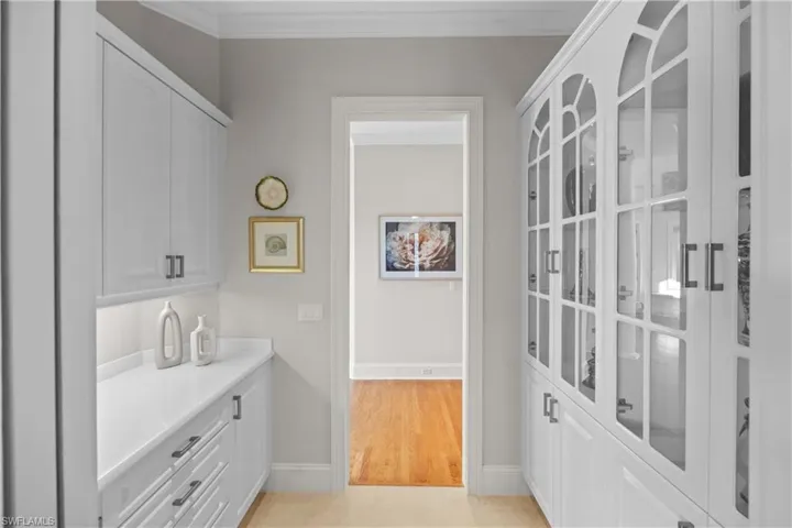 Bar featuring white cabinetry, crown molding, and light hardwood / wood-style flooring