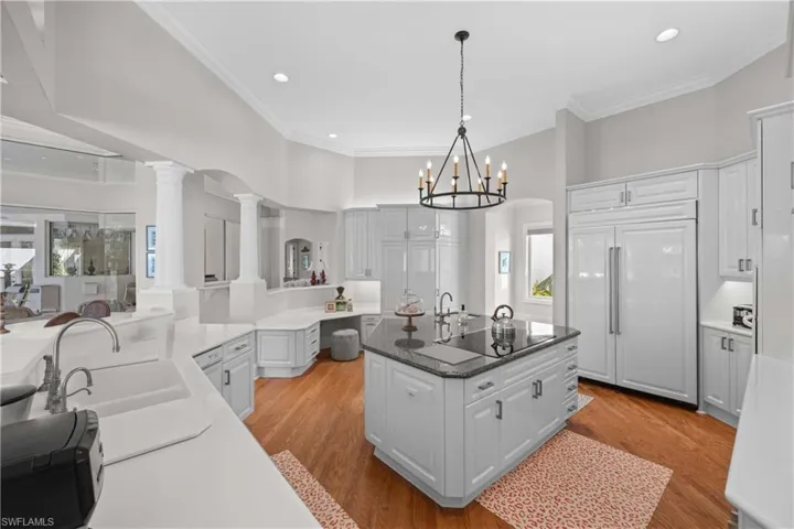Kitchen with ornate columns, a center island, hanging light fixtures, paneled fridge, and light wood-type flooring