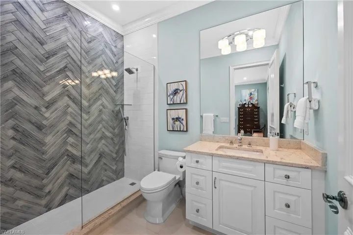 Bathroom with tiled shower, vanity, toilet, and ornamental molding