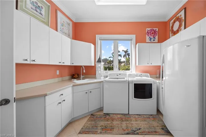Laundry room featuring cabinets, crown molding, sink, light tile patterned floors, and separate washer and dryer