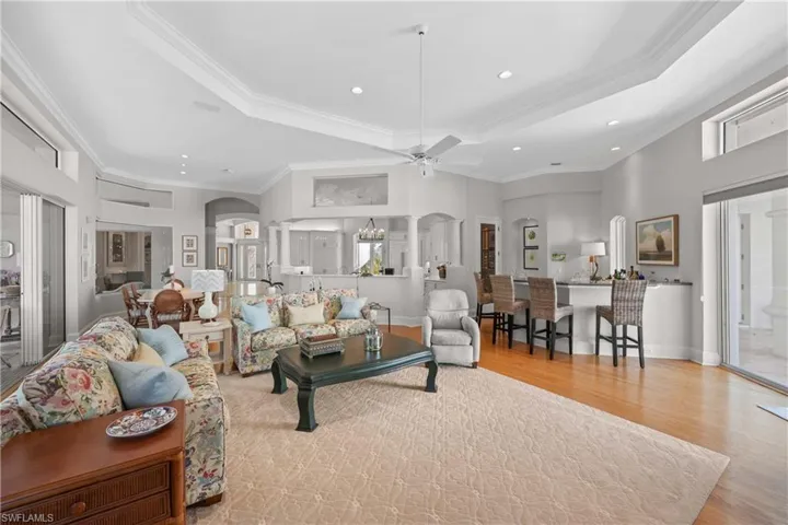 Living room featuring a tray ceiling, crown molding, light hardwood / wood-style floors, and ceiling fan with notable chandelier