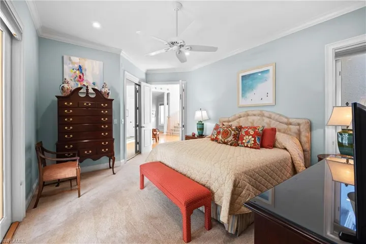 Carpeted bedroom with connected bathroom, ceiling fan, and ornamental molding