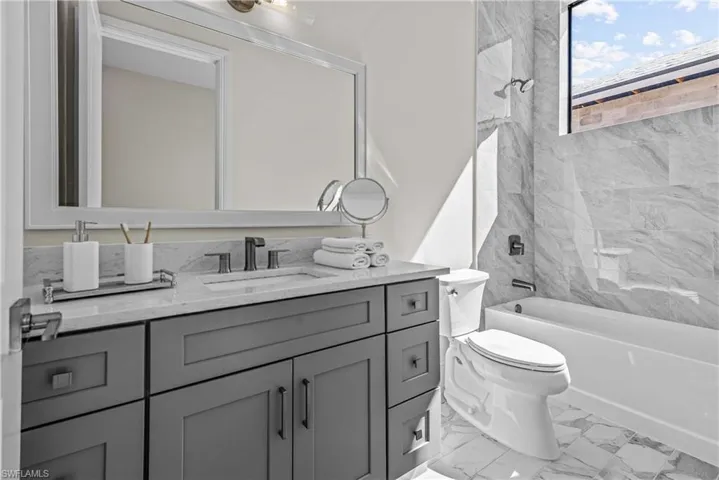 Bathroom with vanity, shower / tub combination, and light marble finish flooring