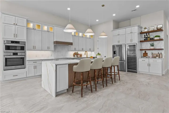 Kitchen featuring backsplash, a kitchen island with sink, hanging light fixtures, a breakfast bar, and beverage cooler
