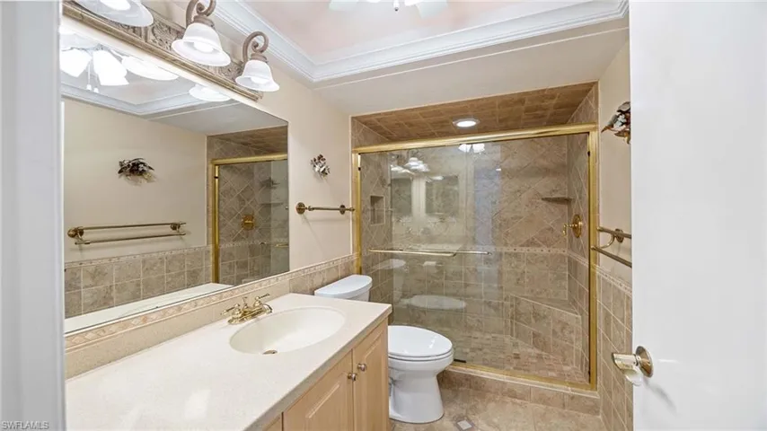 Full bath featuring vanity, a shower stall, ornamental molding, tile walls, and light tile patterned floors