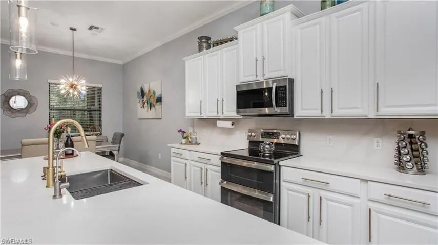 Kitchen featuring appliances with stainless steel finishes, light countertops, white cabinets, a chandelier, and ornamental molding