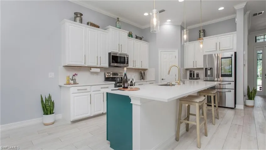 Kitchen featuring stainless steel appliances, a kitchen breakfast bar, white cabinetry, an island with sink, and crown molding