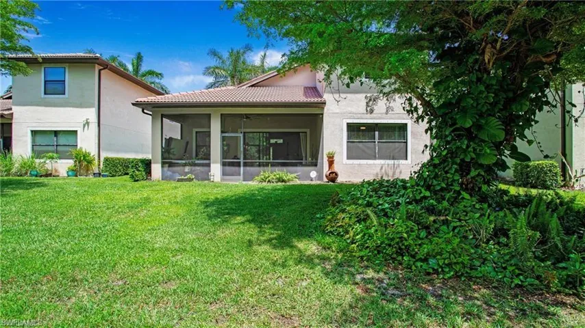 Back of property featuring a tiled roof, a lawn, a sunroom, and stucco siding