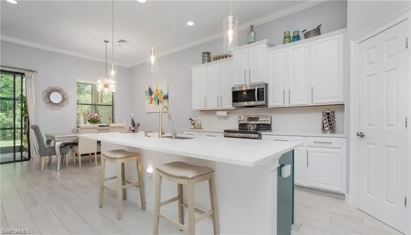 Kitchen with appliances with stainless steel finishes, light countertops, a kitchen island with sink, white cabinetry, and ornamental molding