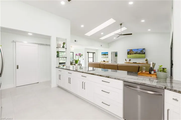 Kitchen featuring stone countertops, white cabinetry, stainless steel dishwasher, vaulted ceiling, and recessed lighting
