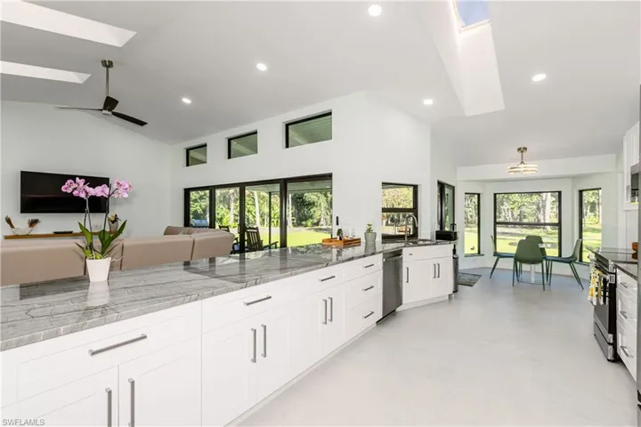 Open floor plan with Vaulted ceilings, skylights, white cabinetry, quartzite stone counters, and recessed lighting