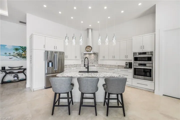 Kitchen with a towering ceiling, backsplash, a kitchen bar, white cabinets, and hanging light fixtures