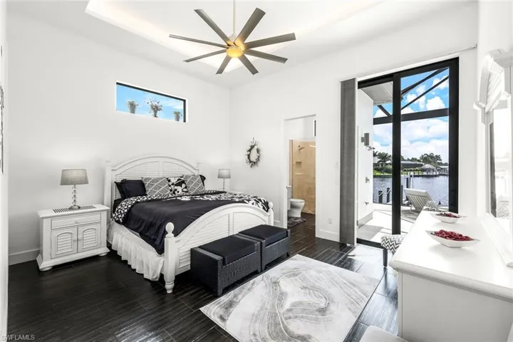 Bedroom featuring dark wood-type flooring, access to exterior, ceiling fan, and a water view