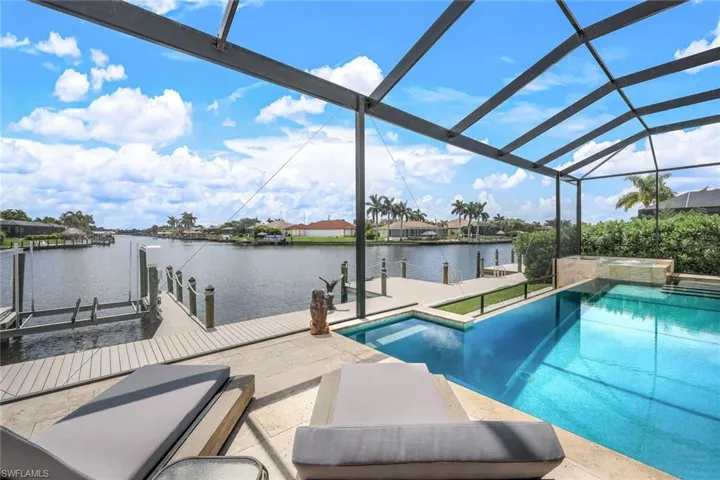 View of swimming pool featuring boat lift, a dock, a water view, a sunroom, and a pool with connected hot tub