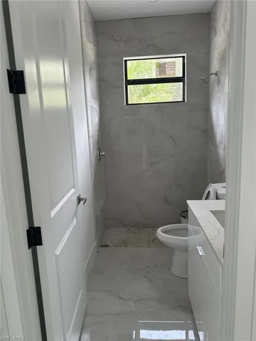Bathroom featuring tile patterned flooring, toilet, vanity, and a tile shower
