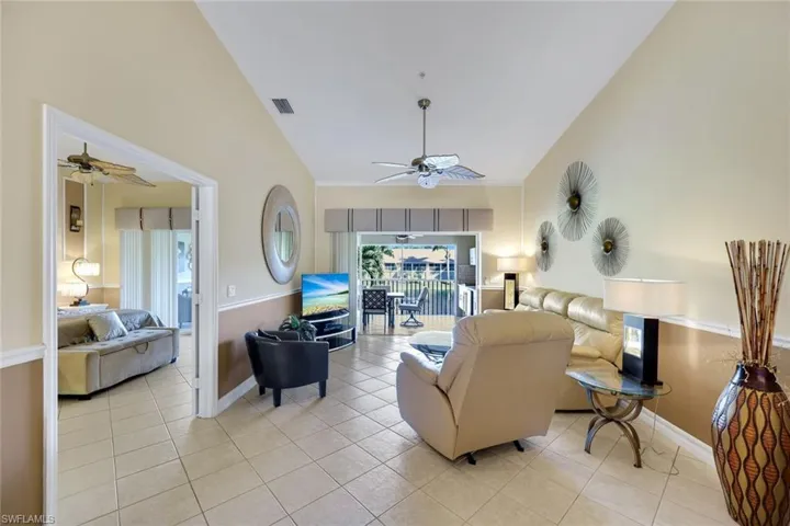 Vaulted ceilings, neutral tile flooring, ceiling fan with light fixture, chair rail molding, and wide sliding glass doors