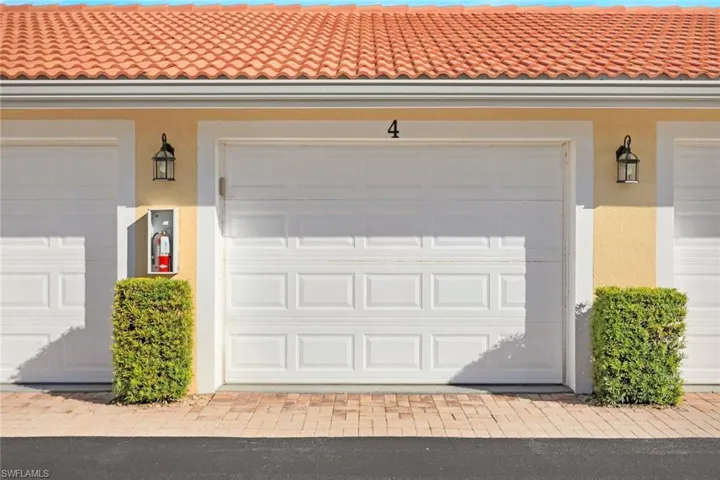 Garage exterior featuring a terracotta-style tile roof, stucco finish, white sectional garage door, and wall-mounted exterior lanterns
