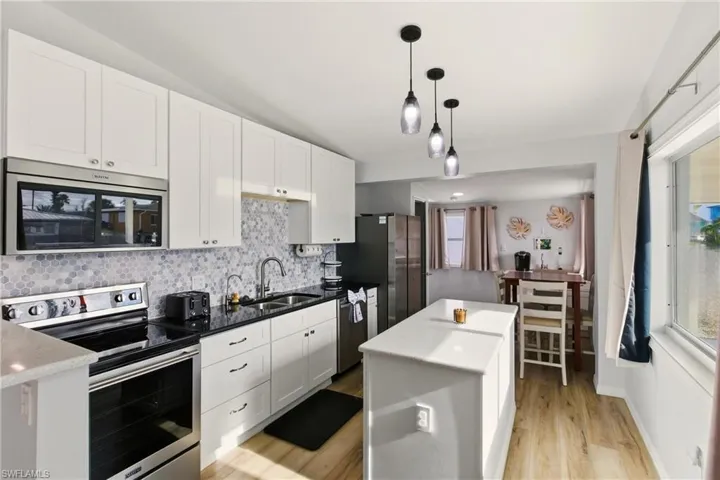 Kitchen featuring stainless steel appliances, white cabinetry, pendant lighting, decorative backsplash, and a center island