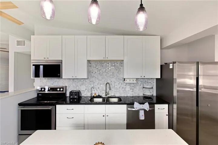 Kitchen with stainless steel appliances, white cabinets, tasteful backsplash, and vaulted ceiling