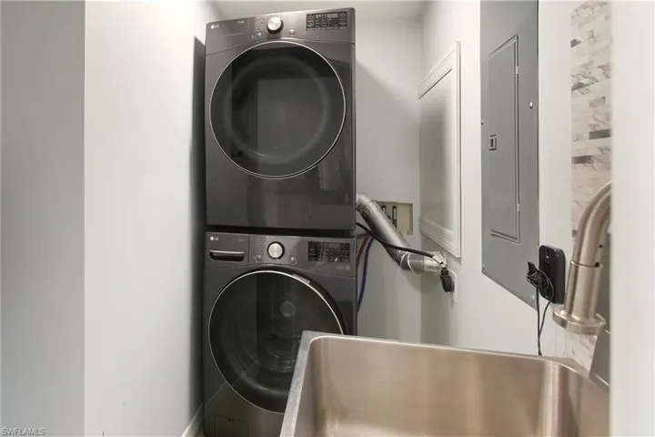 Laundry room featuring electric panel and stacked washer / dryer