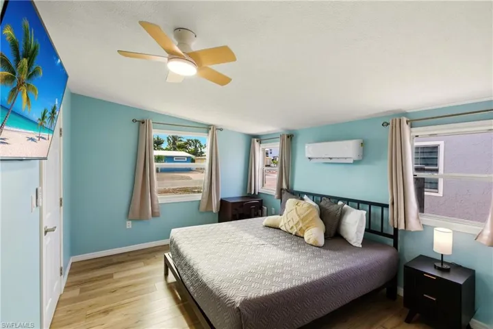 Bedroom featuring lofted ceiling, a textured ceiling, light wood-type flooring, a ceiling fan, and a wall unit AC