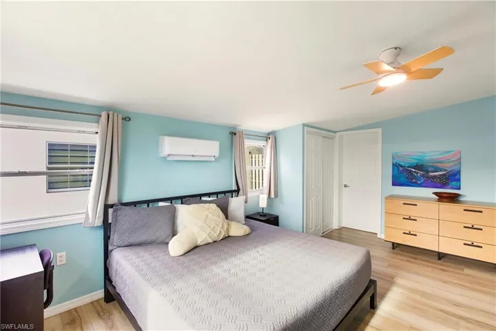 Bedroom with light wood-style flooring, lofted ceiling, ceiling fan, and an AC wall unit