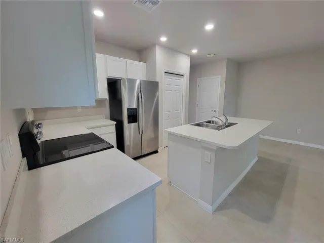 Kitchen with stove, a center island with sink, sink, light tile patterned floors, and stainless steel refrigerator with ice dispenser