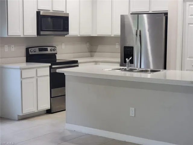 Kitchen featuring light tile patterned flooring, stainless steel appliances, white cabinets, sink, and a center island
