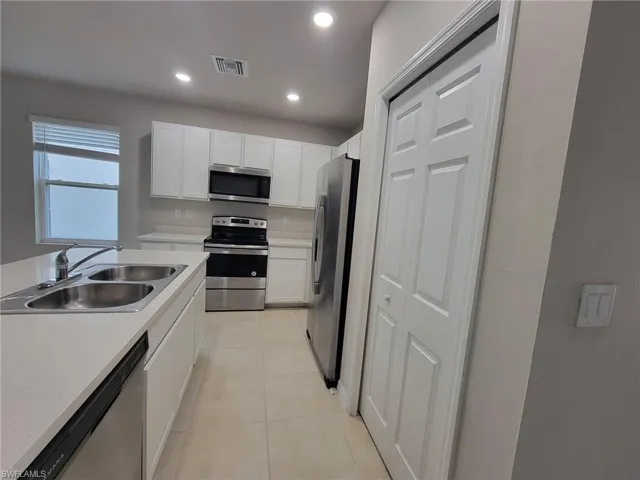 Kitchen featuring light tile patterned flooring, sink, stainless steel appliances, and white cabinets