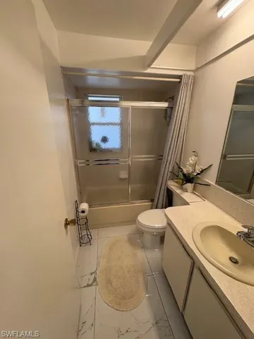 Full bath with enclosed tub / shower combo, vanity, and light marble finish flooring