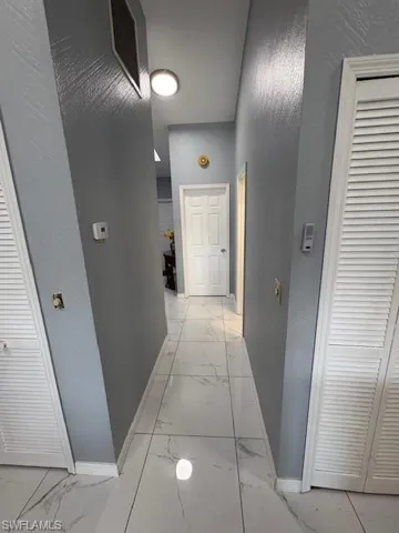 Hall with light marble finish flooring and a textured wall