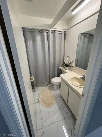 Bathroom with curtained shower, vanity, and light marble finish flooring